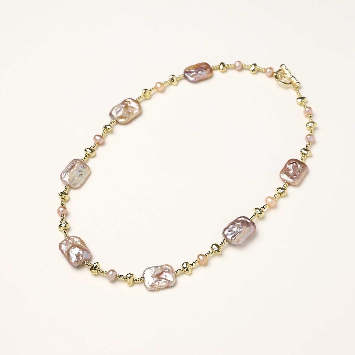 Long gold-plated necklace with iridescent baroque pearls and round freshwater pearls on cream background