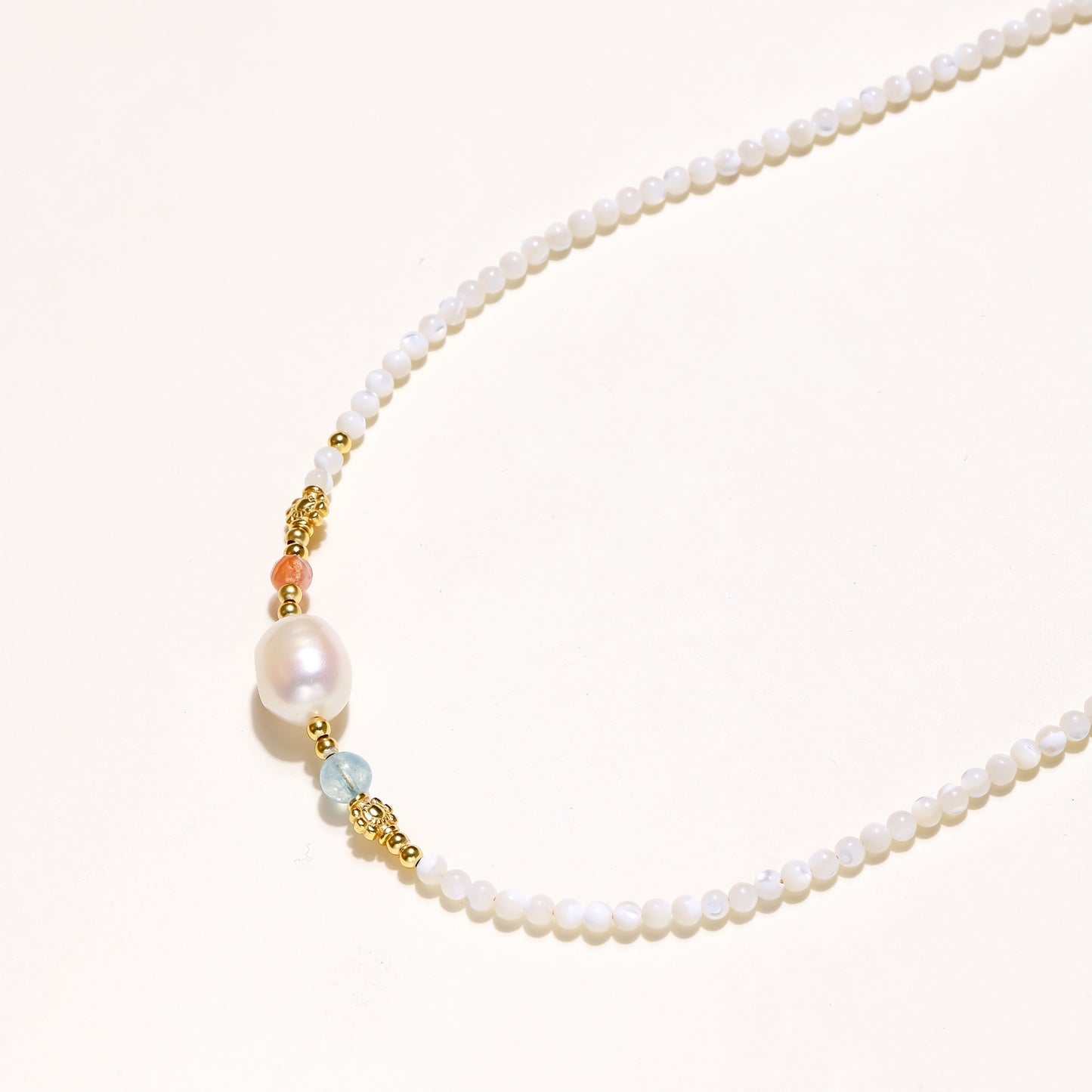 Delicate white beaded necklace with central freshwater pearl and gold-toned emerald accents on white background.
