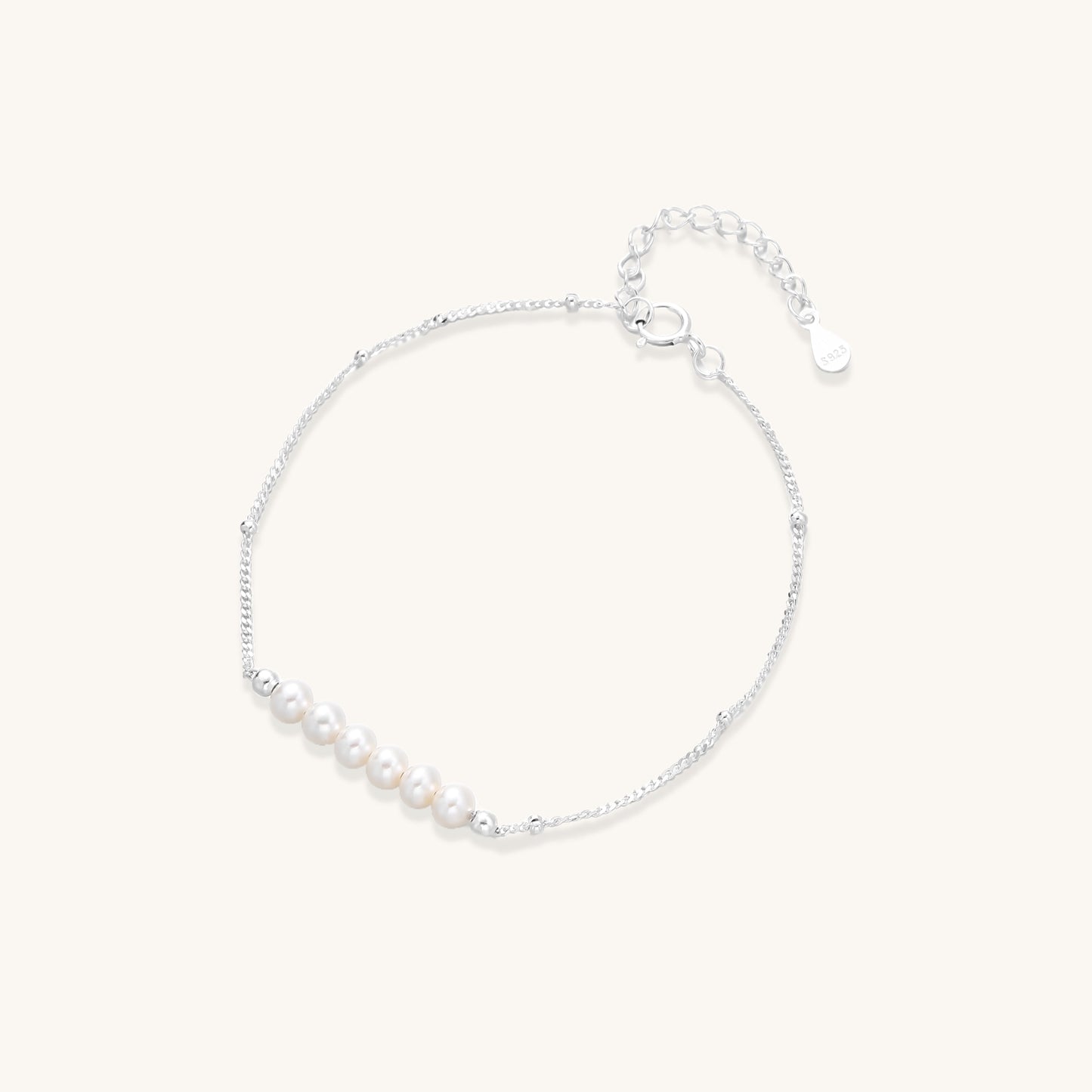 Dainty sterling silver bracelet with small white baroque pearls and adjustable chain on neutral background.
