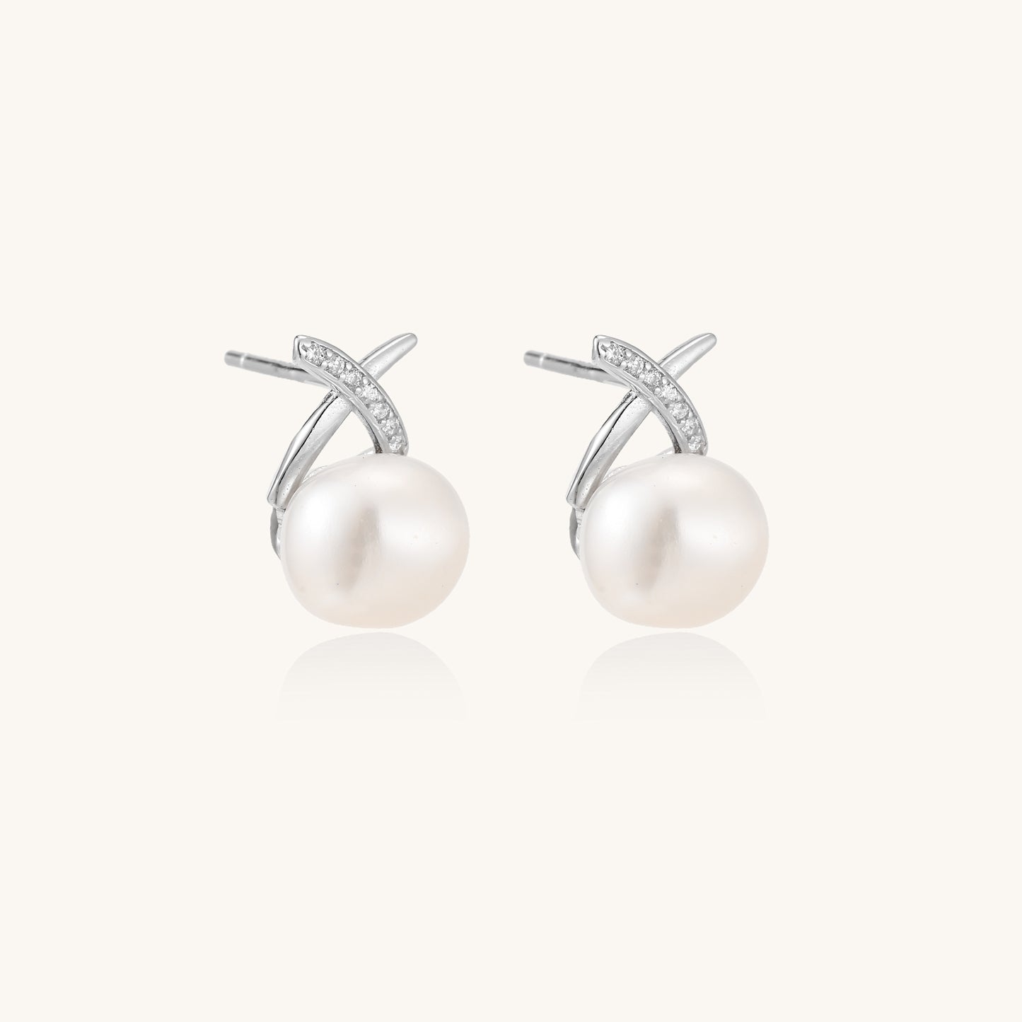 Sterling silver cross-shaped stud earrings with round freshwater pearls dangling below on white background.