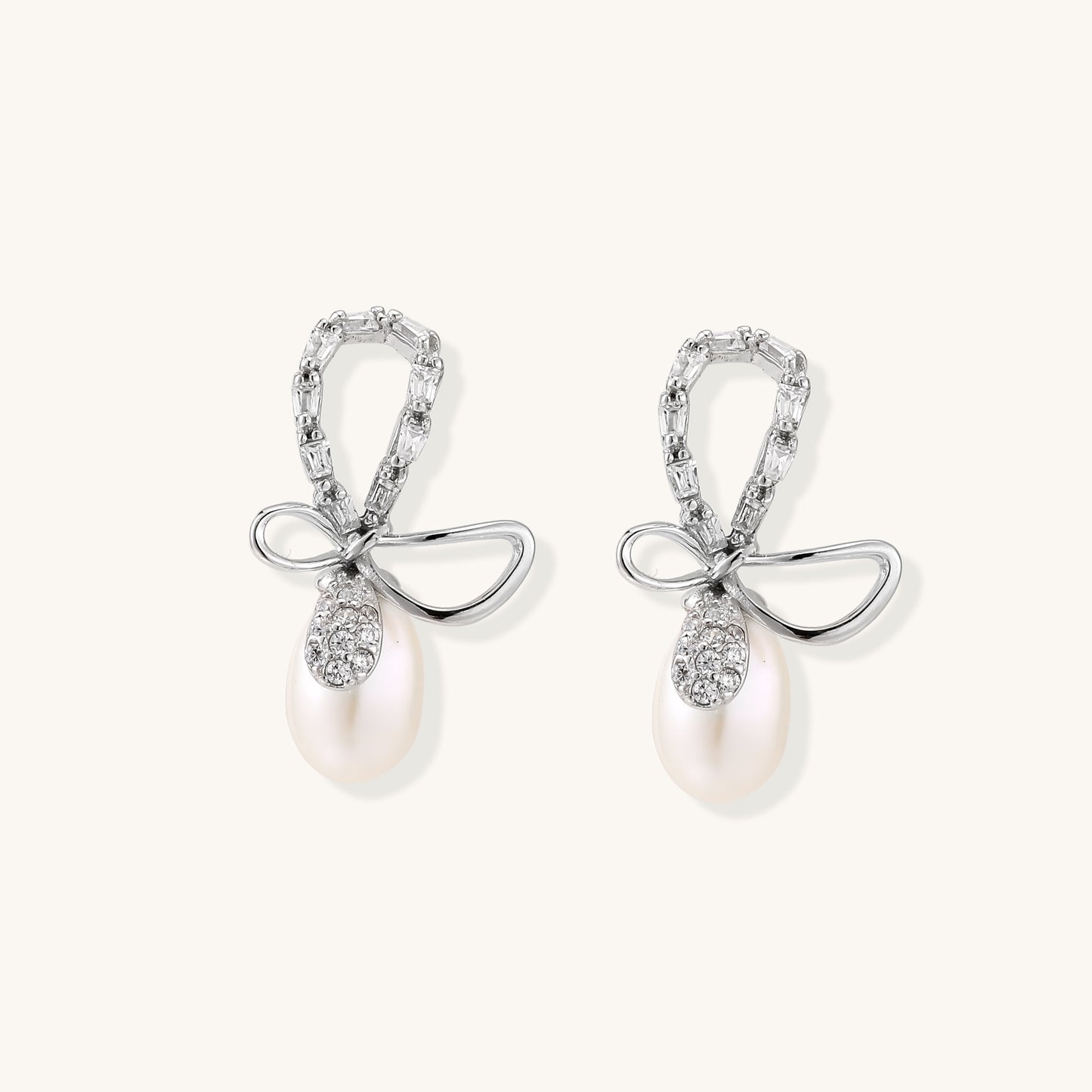 Sterling silver stud earrings with baguette crystal bow design and freshwater pearl drops on white background