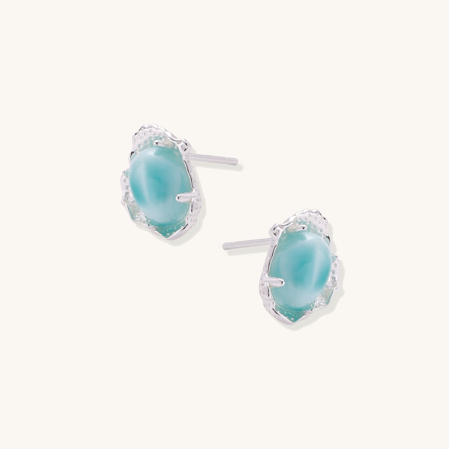 Close-up of sterling silver stud earrings with oval larimar stones in flowing wave-like settings on white background.