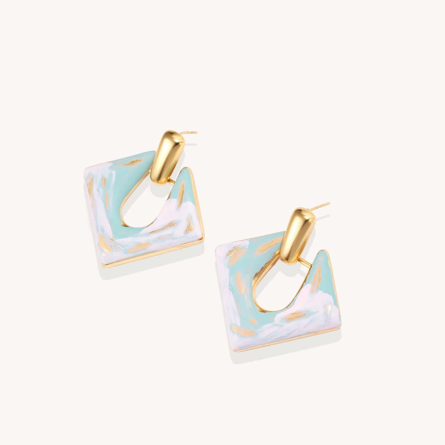 Diamond-shaped gold-plated earrings with pastel marble enamel in turquoise and lavender swirls on beige background