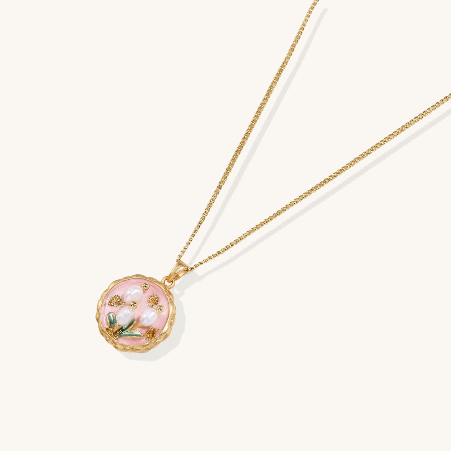 Gold-plated pendant necklace with pink enamel background and white freshwater pearl floral design on neutral background.