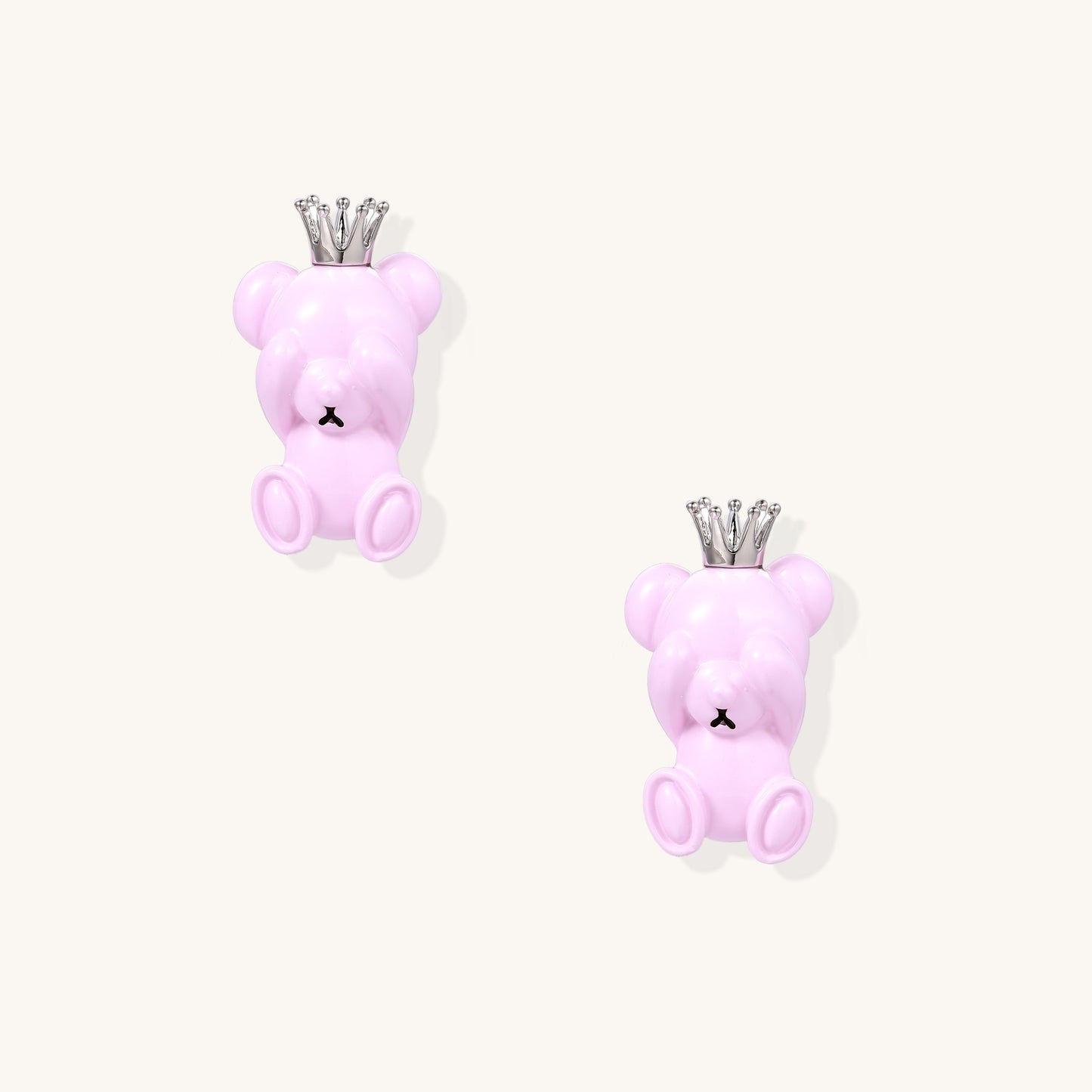Pair of pink teddy bear-shaped stud earrings with silver crowns on white background, made from gold-plated brass