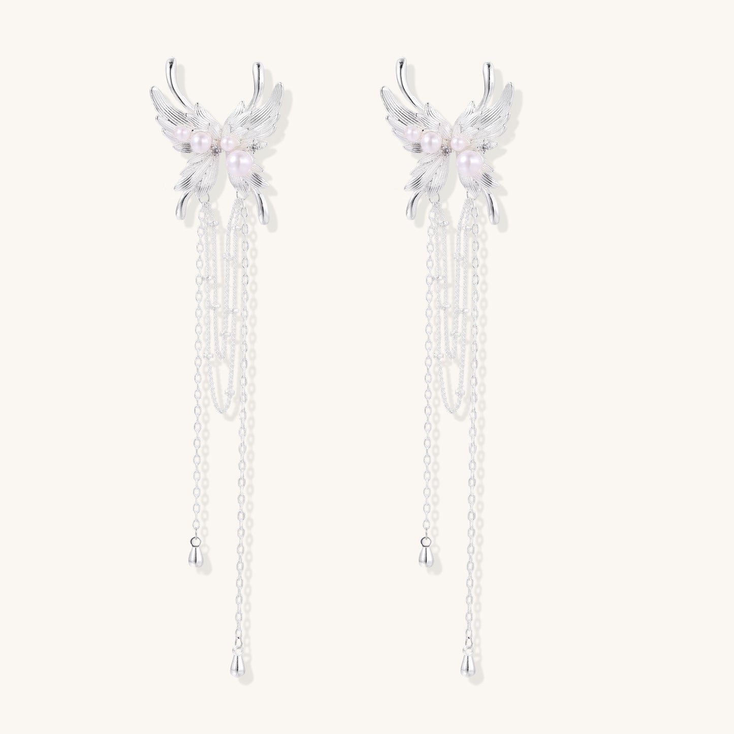 Elegant silver-plated drop earrings with wing-shaped tops, white pearl accents, and long chain tassels on white background.