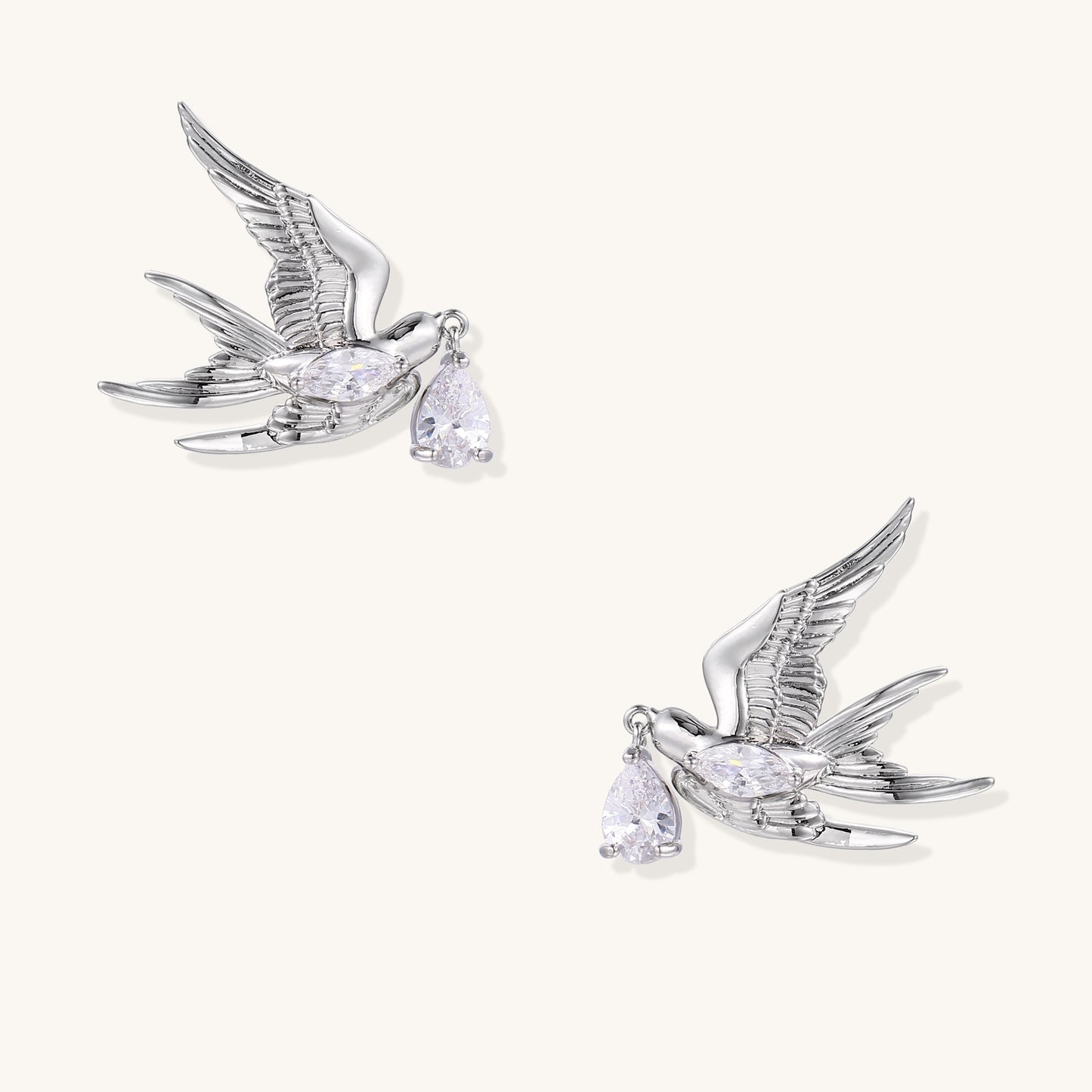 Gold-plated brass swallow earrings with detailed wing engravings carrying clear zirconia crystal drops in their beaks