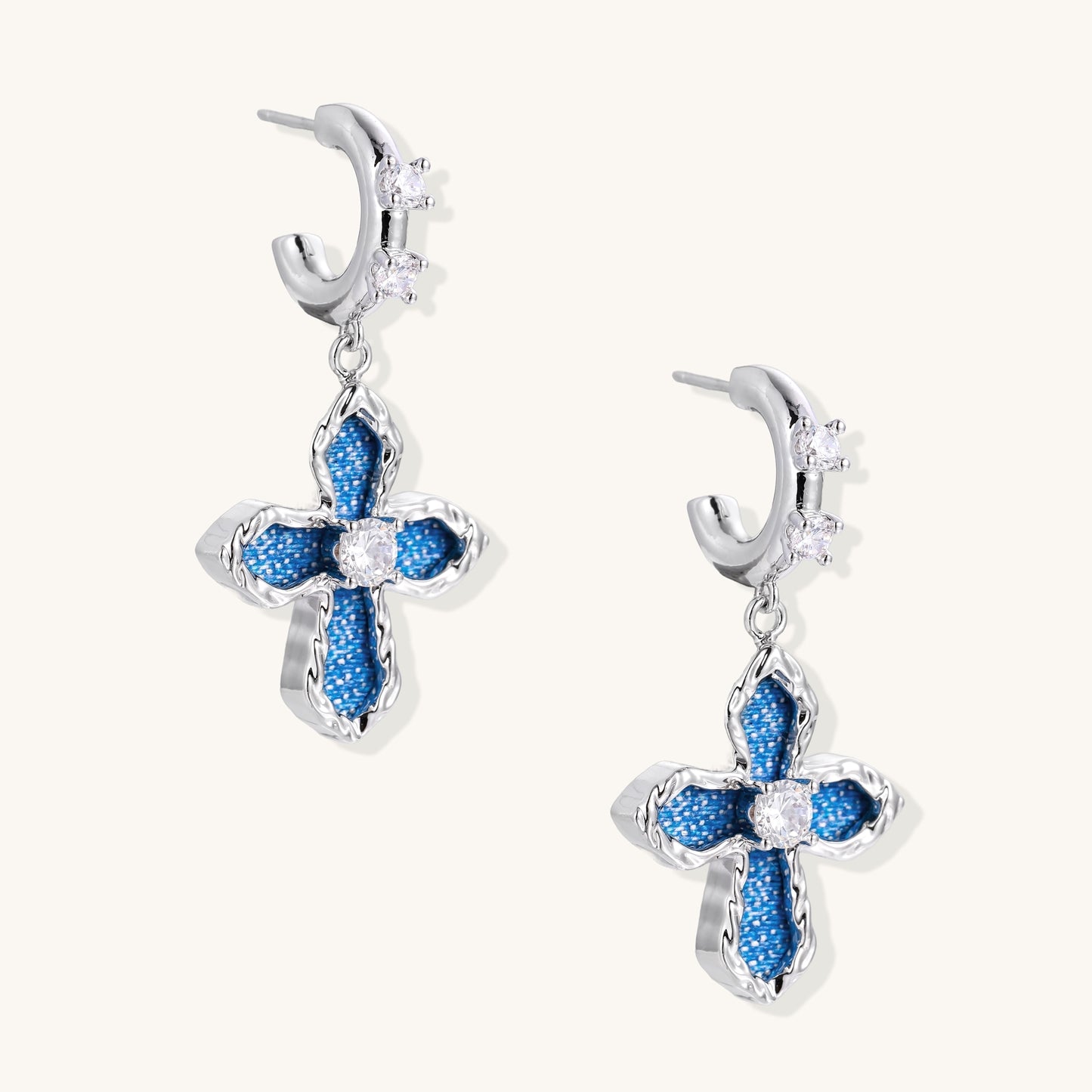 Gold-plated huggie earrings with blue denim-textured cross charms and clear zirconia center stones on white background.