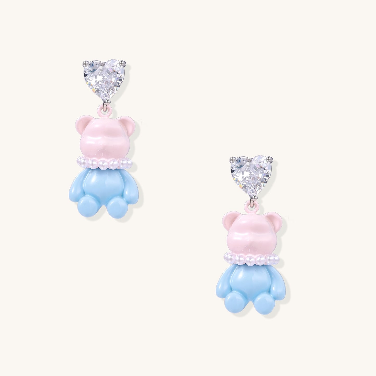 Cute teddy bear earrings with heart-shaped crystals, gold plating, and white pearl accents in pink and blue variants
