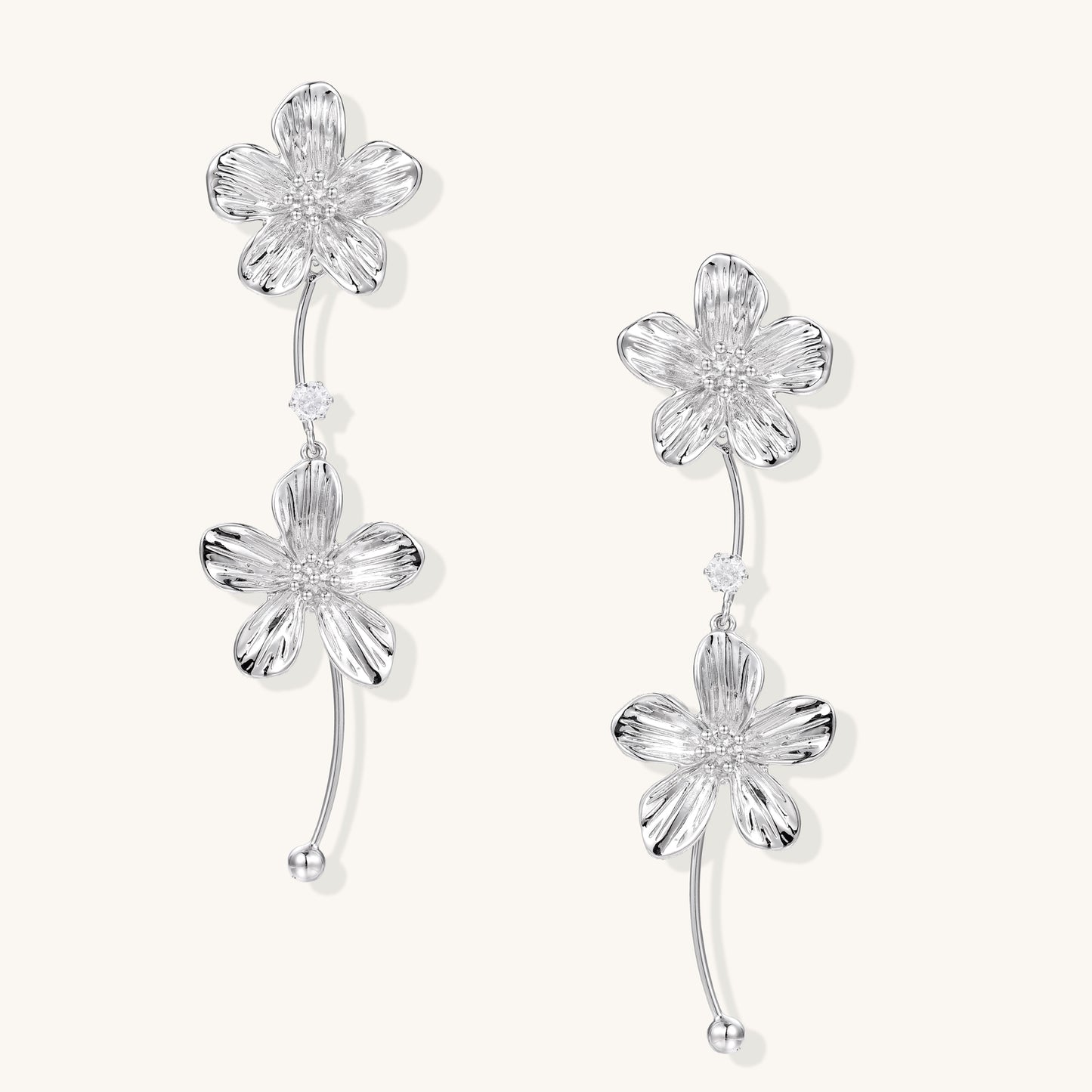 Gold-plated floral dangle earrings with zirconia crystal centers and curved stems on white background.