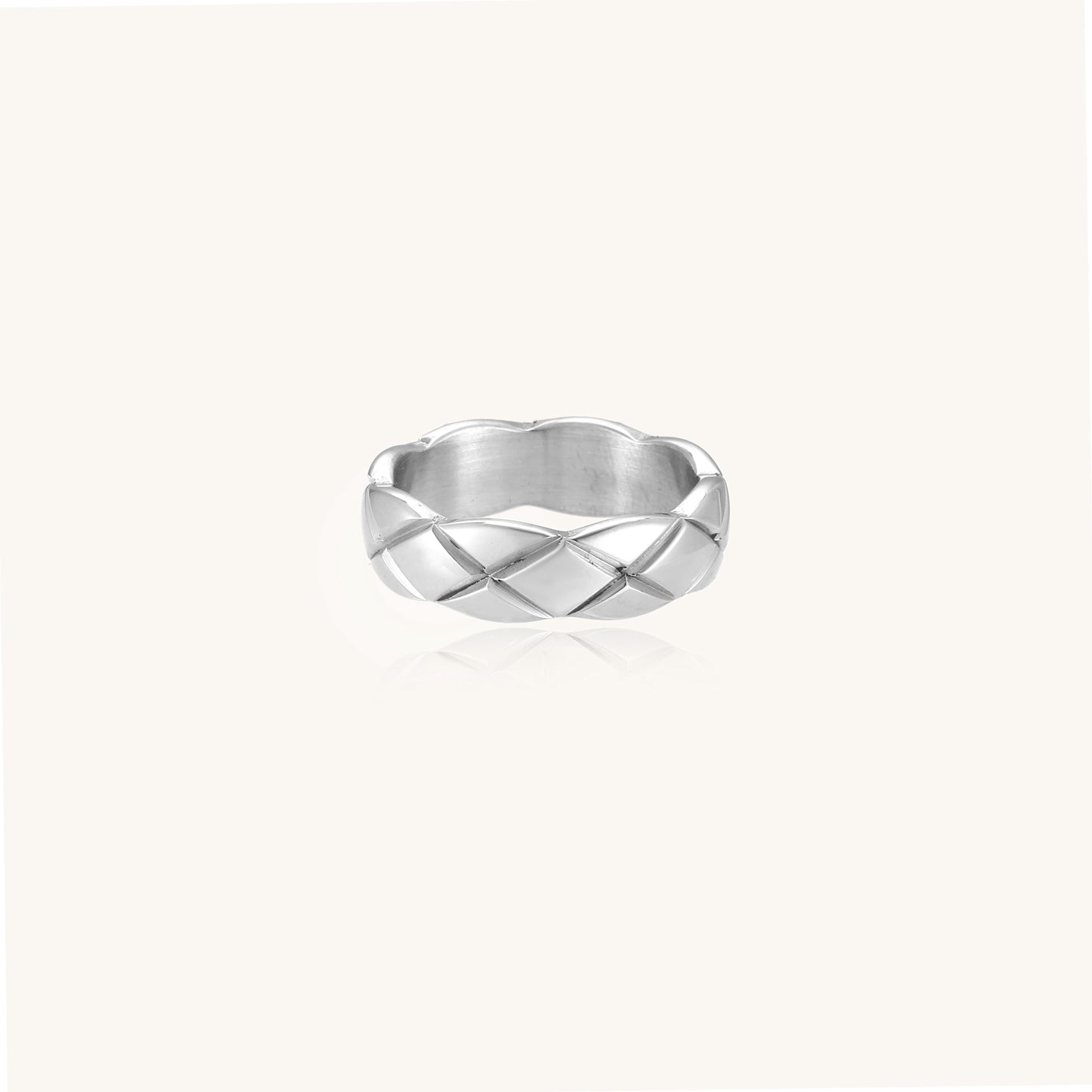 Close-up of a polished stainless steel ring featuring a geometric quilted diamond pattern on white background.
