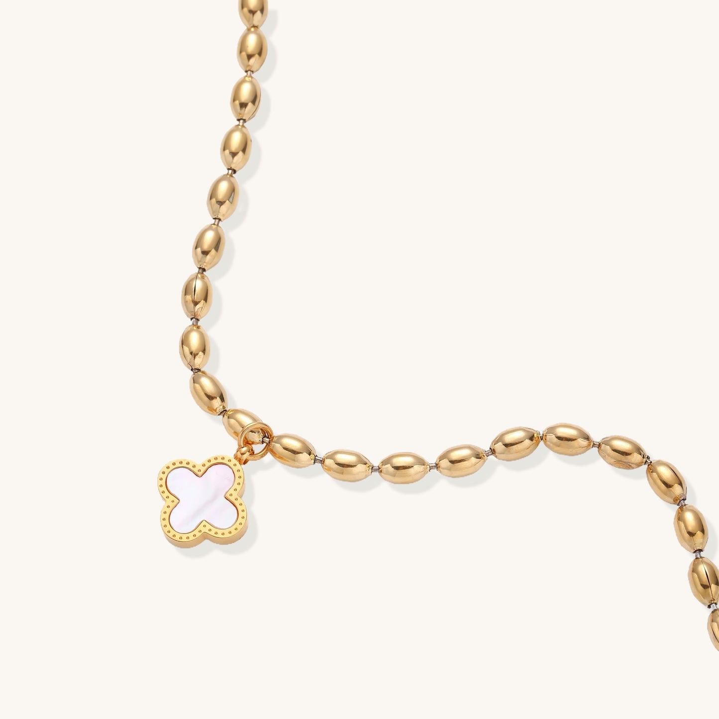 Dainty gold-plated beaded bracelet with oval links and four-leaf clover charm pendant on neutral background.