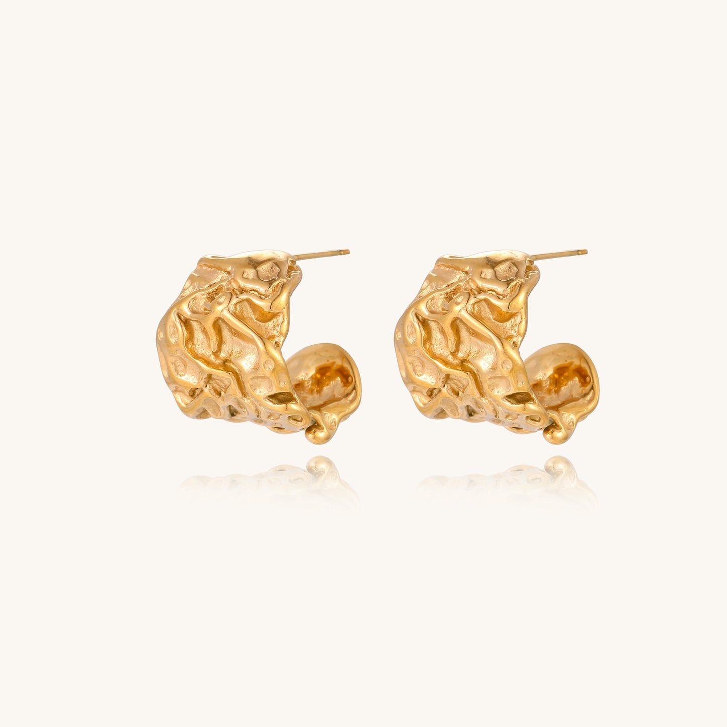 Textured gold-plated hoop earrings with organic molten surface pattern on cream background, showing intricate flowing details.