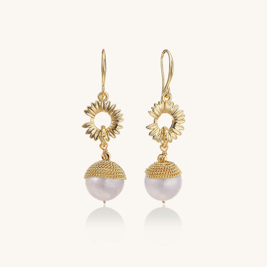 Gold-plated sunburst flower earrings with baroque pearl drops and textured metal caps on neutral background.