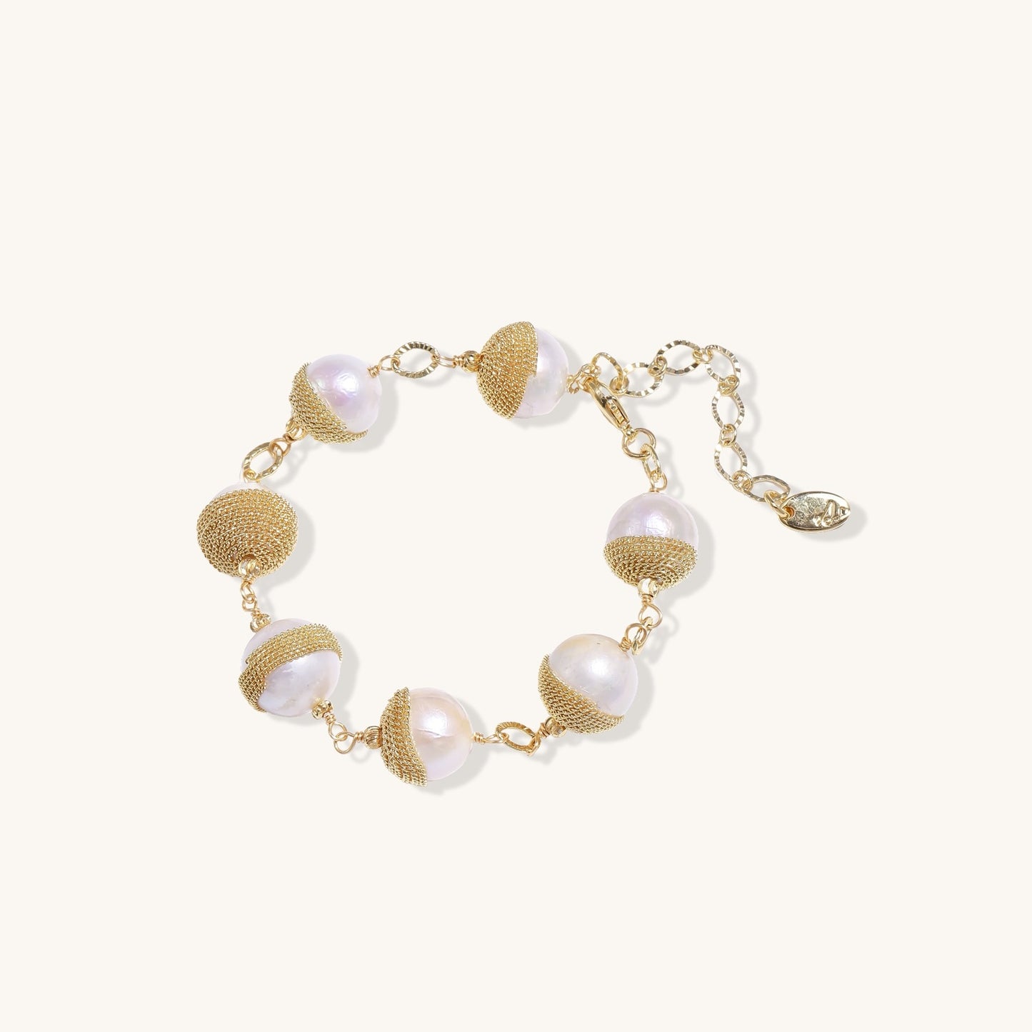 Adjustable bracelet featuring baroque pearls wrapped in gold mesh wire with delicate chain links on cream background.