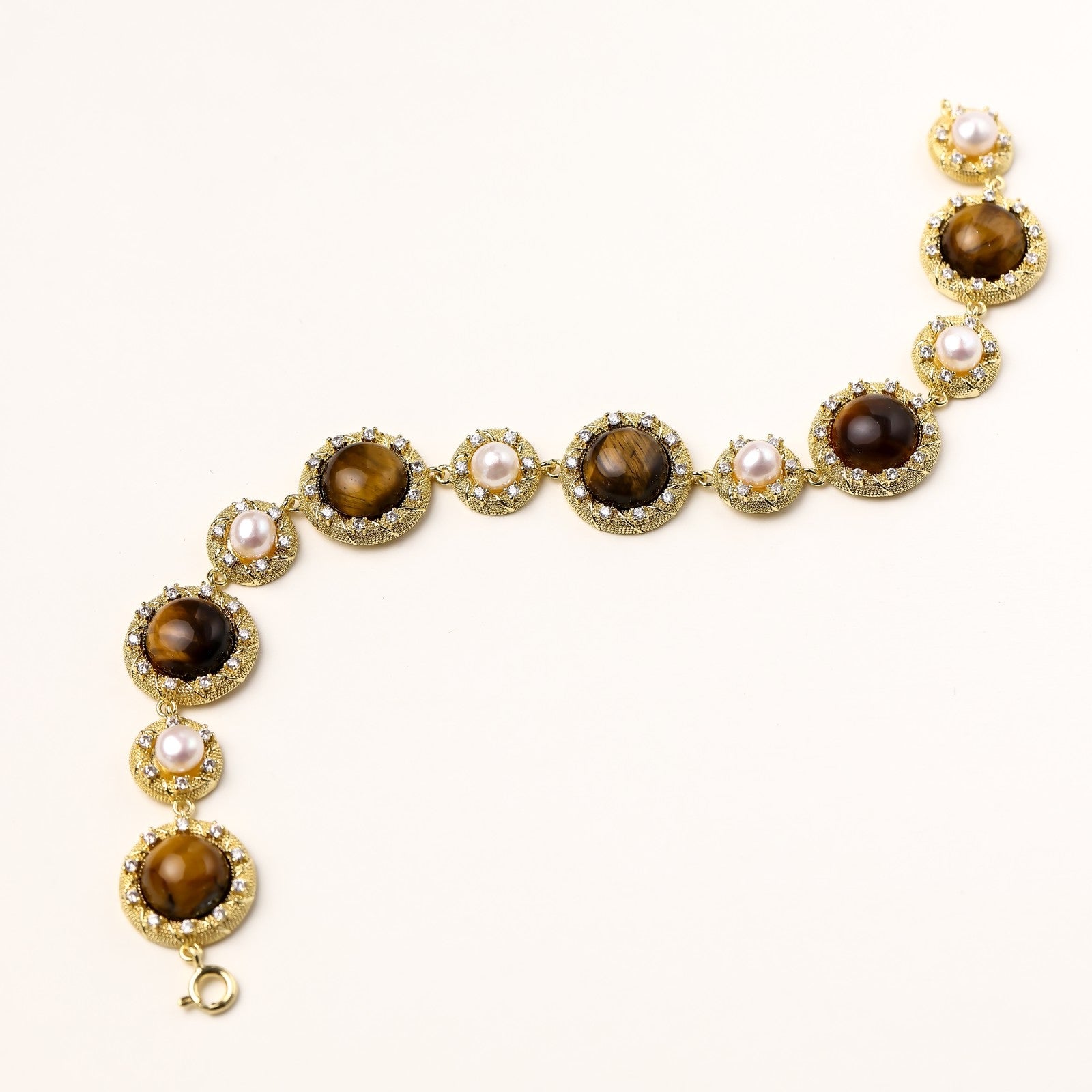 Ornate gold-plated bracelet with alternating brown tiger's eye stones and white freshwater pearls in crystal-accented settings