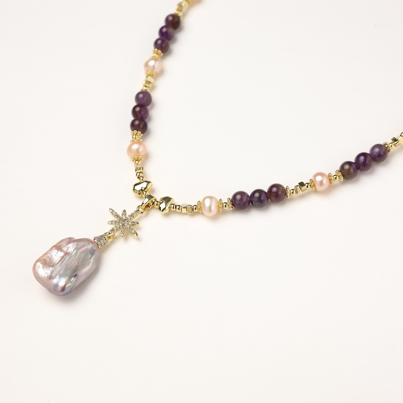 Gold-plated necklace with purple amethyst beads, pink pearls, and iridescent baroque pearl pendant beneath crystal star charm