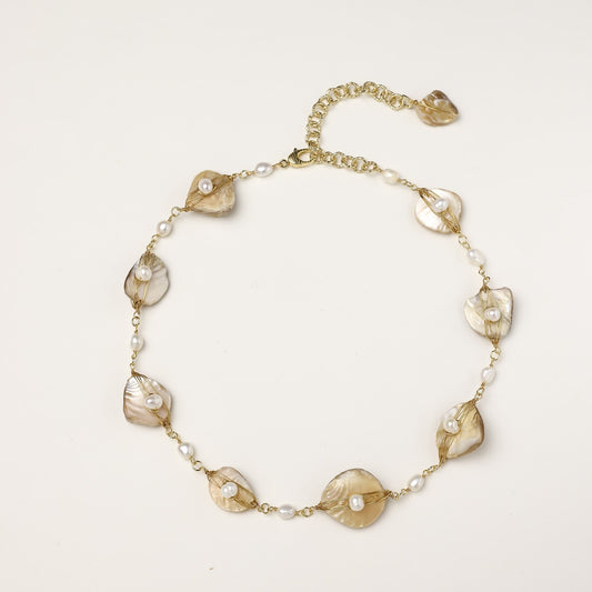 Delicate gold chain bracelet featuring iridescent shell charms with freshwater pearls on white background.