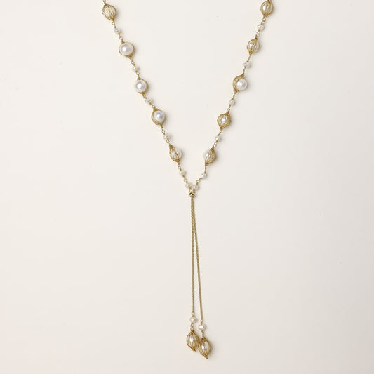 Long gold-plated lariat necklace with wire-wrapped freshwater pearls and chain tassel detail on cream background.
