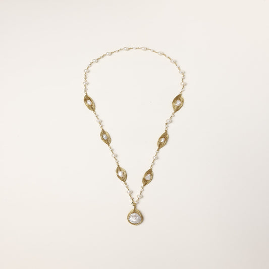 Long gold-plated necklace with eye-shaped elements, freshwater pearls, and baroque pearl pendant on neutral background.