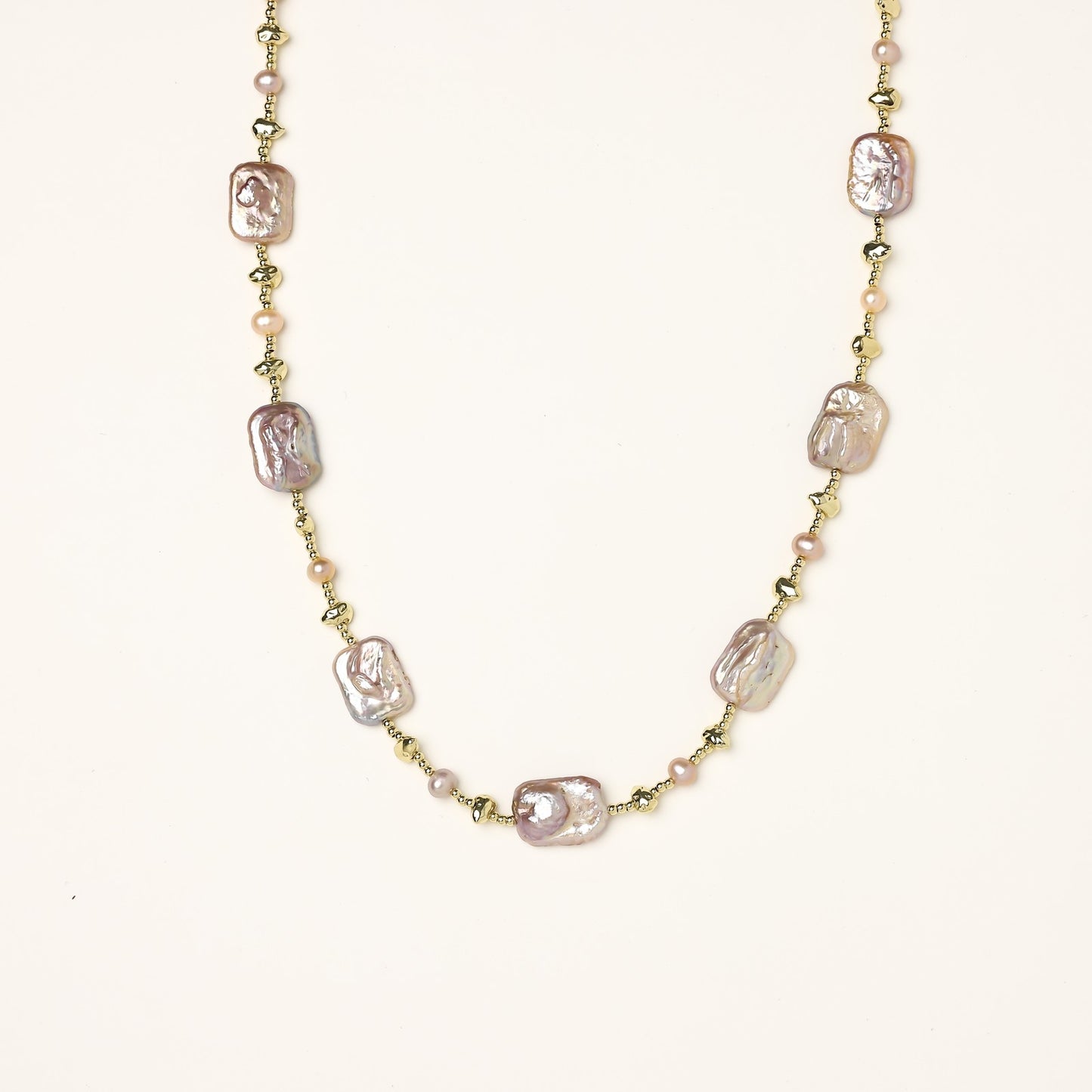 Long gold-plated necklace with iridescent baroque pearls and round freshwater pearls on cream background