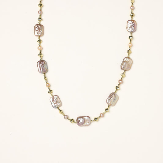Long gold-plated necklace with iridescent baroque pearls and round freshwater pearls on cream background