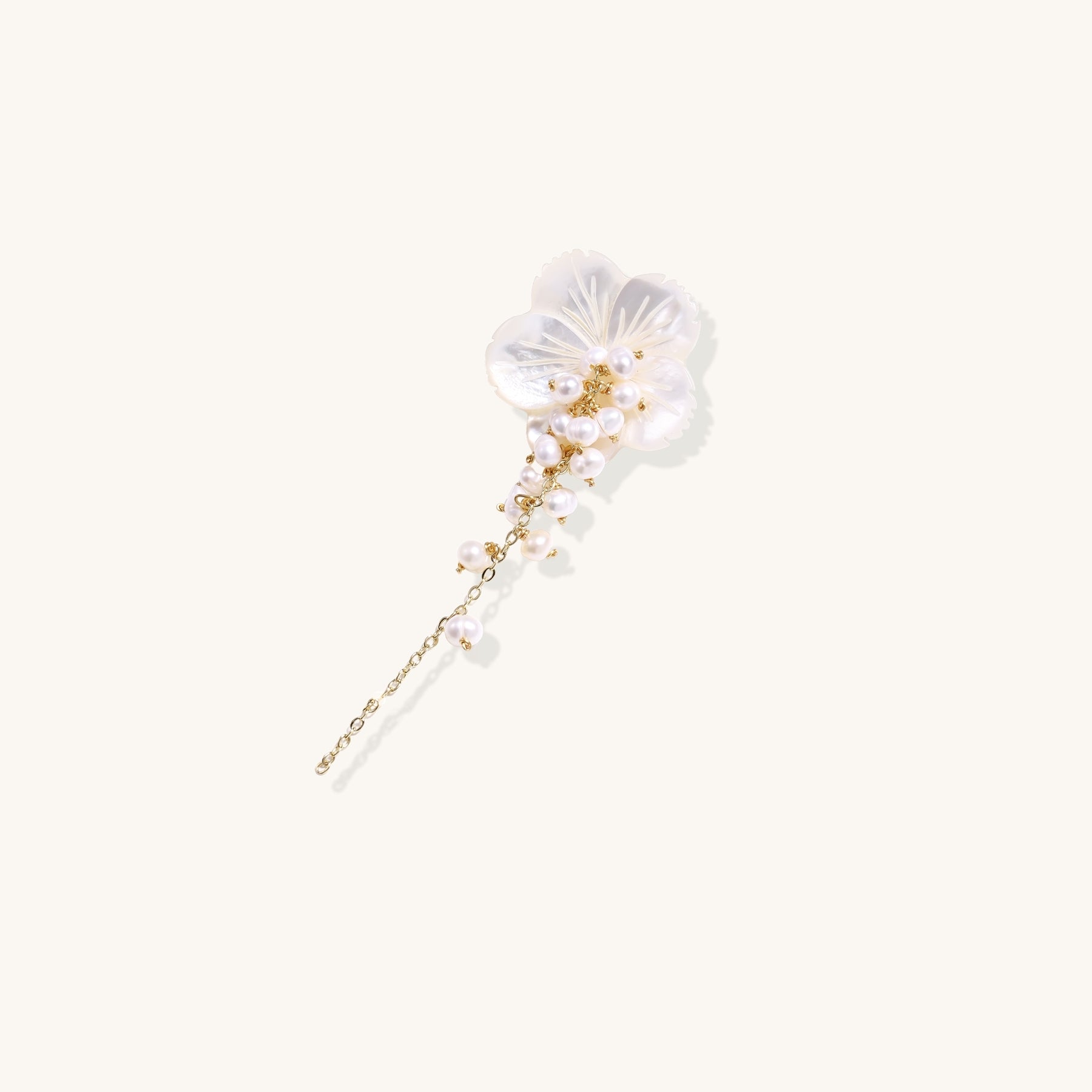 Delicate hair pin featuring translucent shell flower with cascading freshwater pearls on gold chain against cream background.