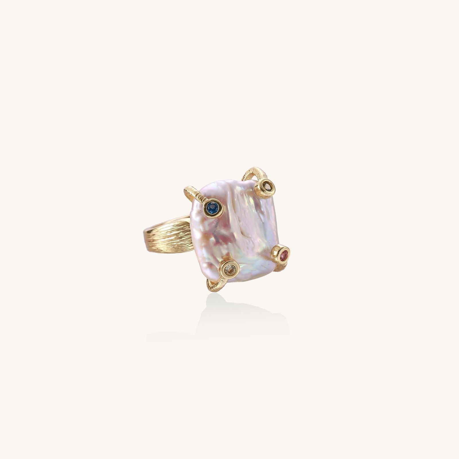 Gold-plated ring featuring large baroque freshwater pearl with small colorful gemstone accents on textured band