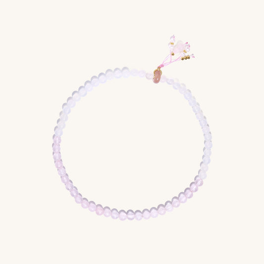 Stretchable bracelet with pink rose quartz and white agate beads, featuring a decorative tassel pendant on white background.