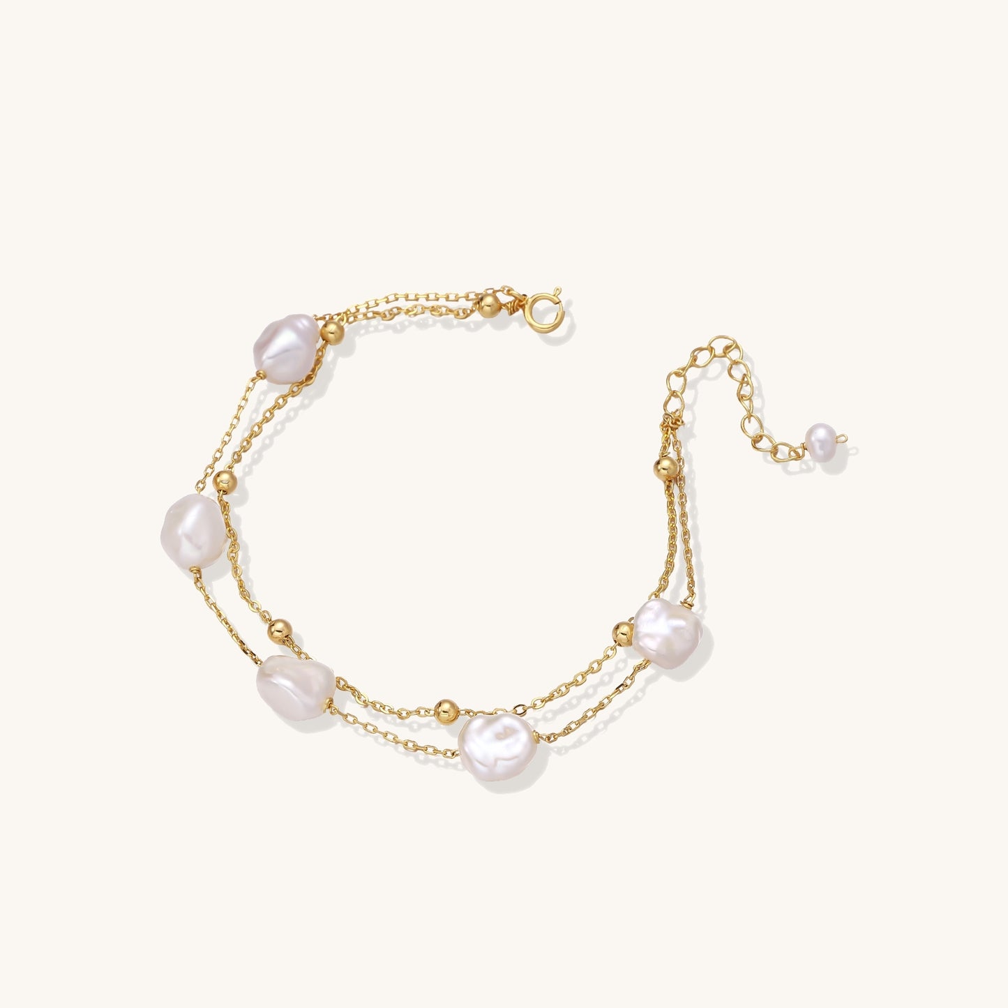 Delicate multi-layered gold-plated bracelet with irregular baroque pearls and freshwater pearls on cream background.