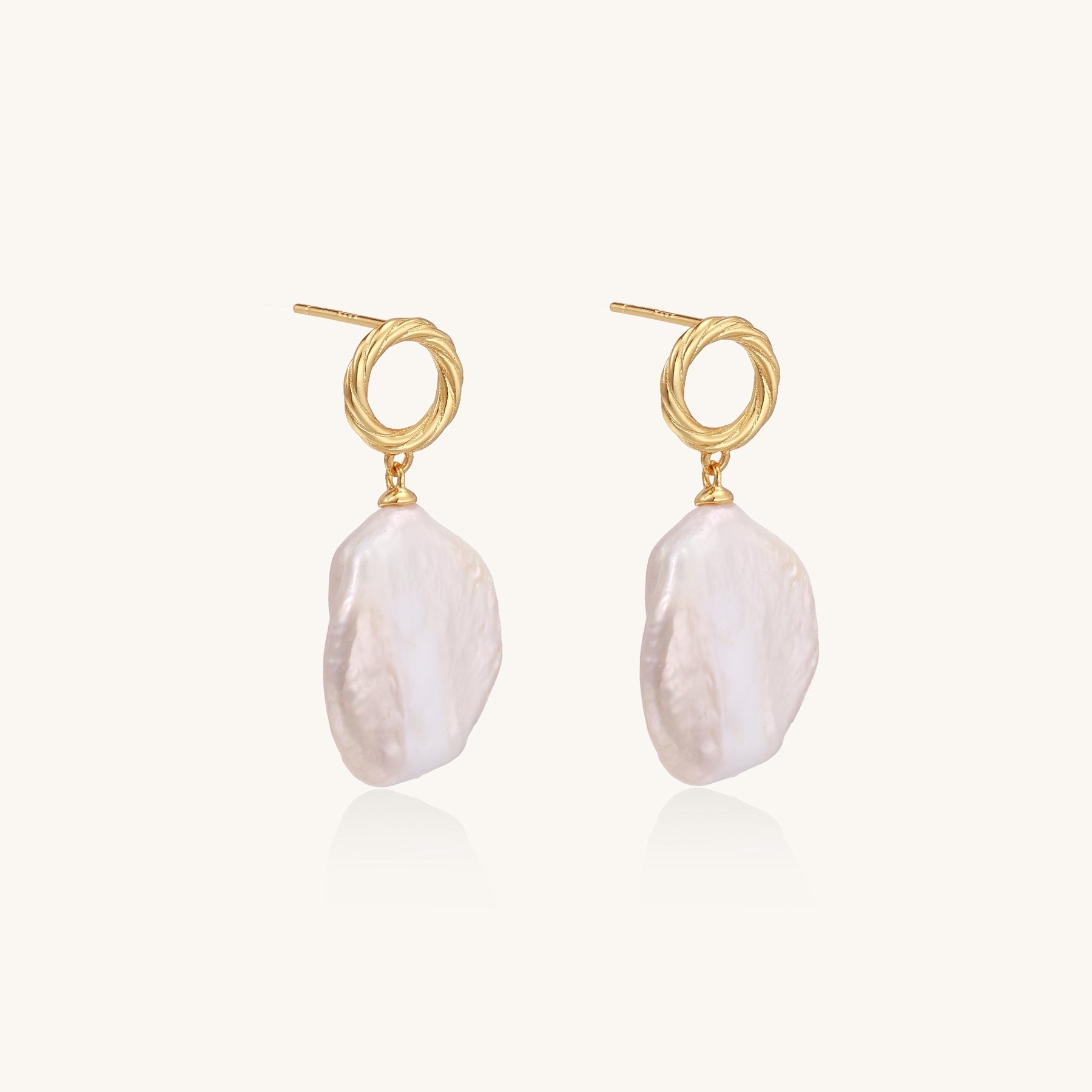 Gold-plated twisted stud earrings with large blush baroque pearls hanging elegantly on white background.