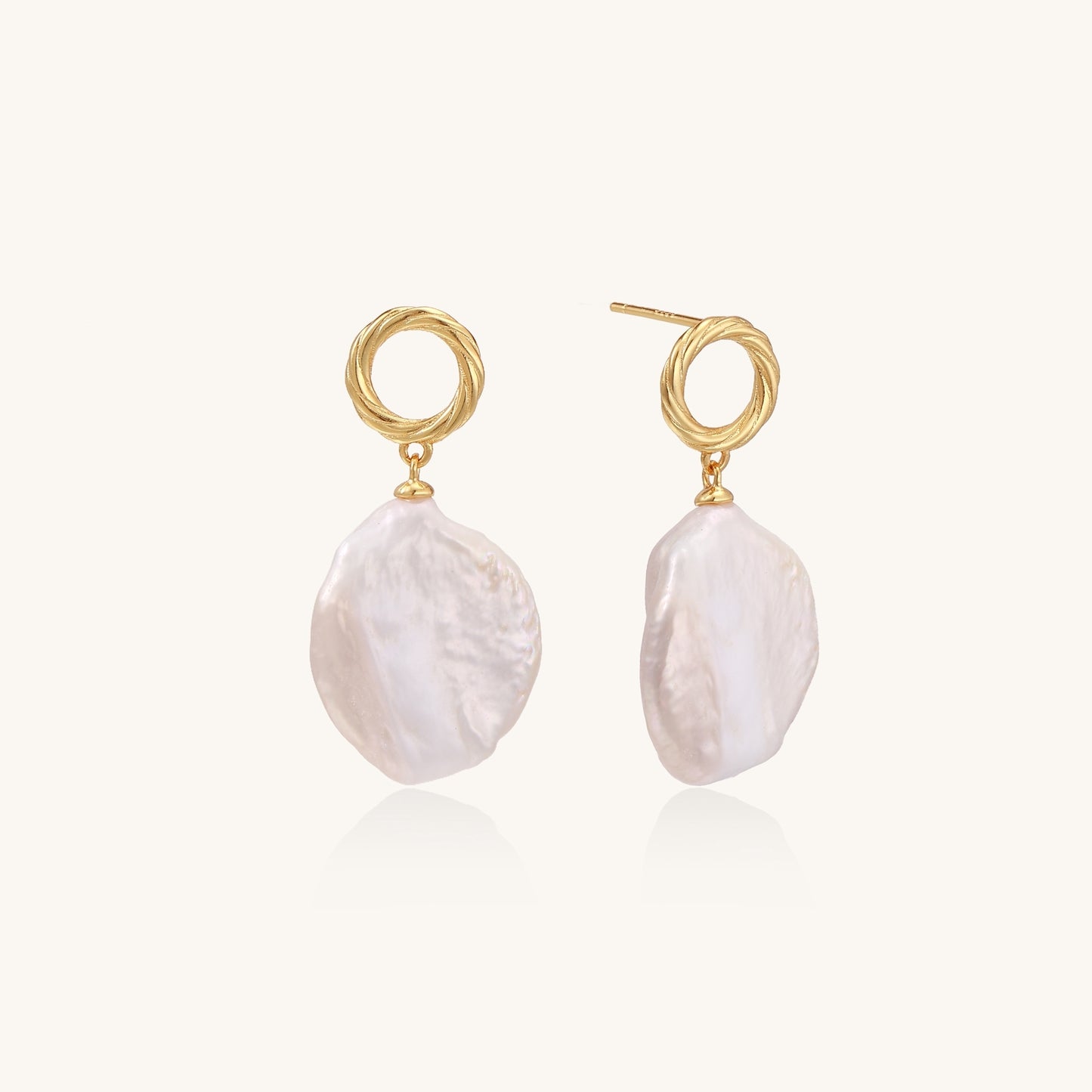 Gold-plated twisted stud earrings with large blush baroque pearls hanging elegantly on white background.