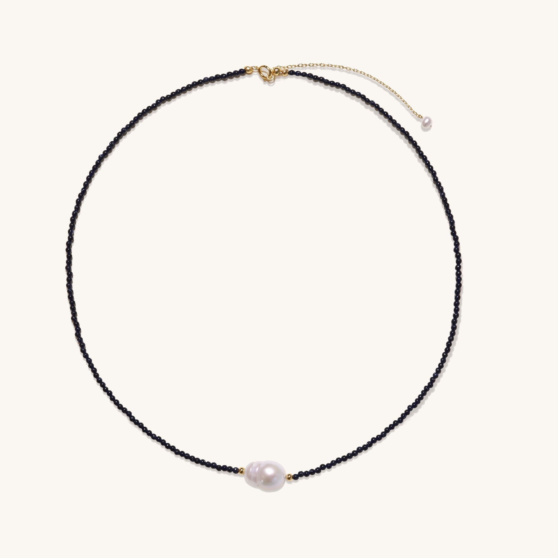 Elegant necklace with blue sandstone beads and baroque pearl centerpiece with gold accents on neutral background.