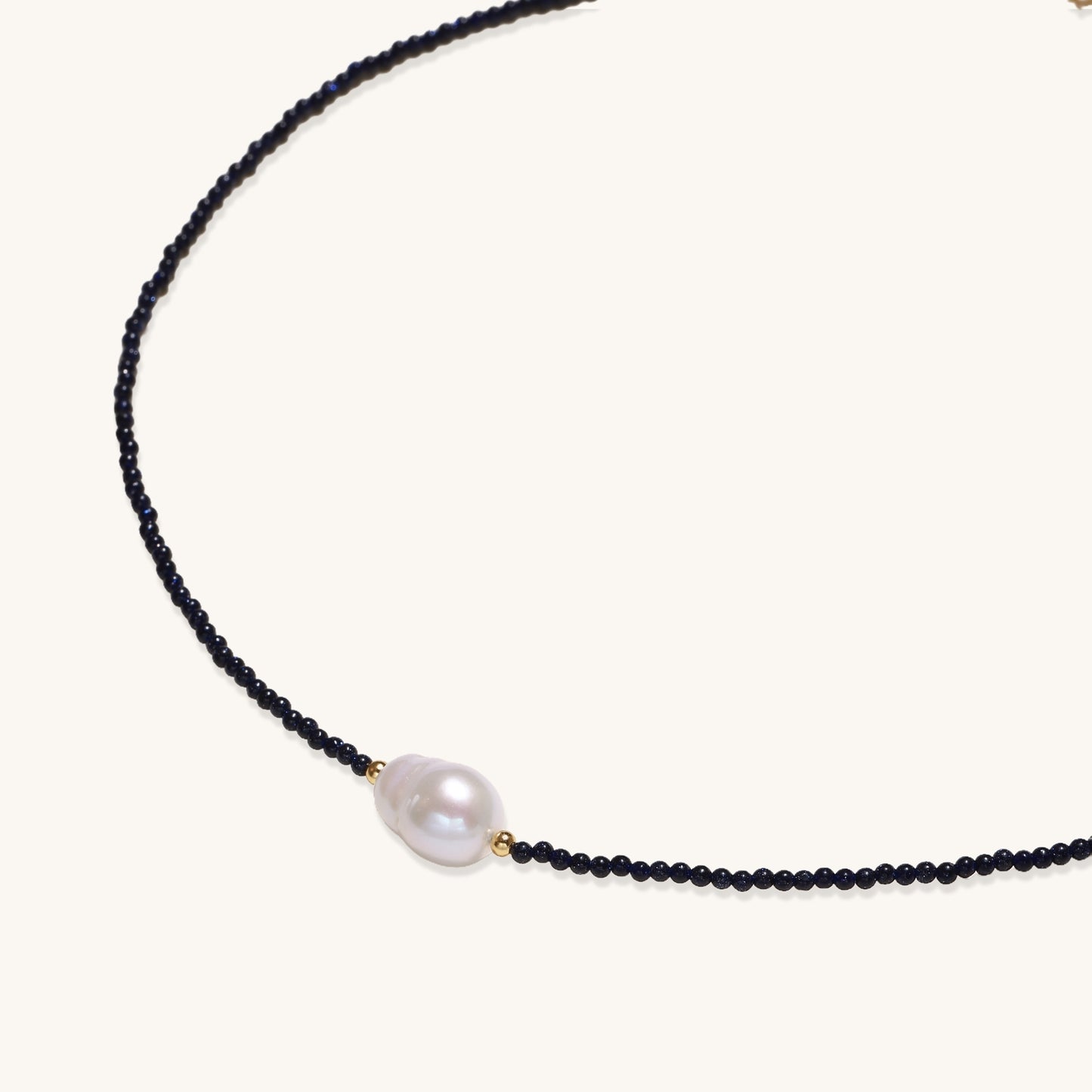 Elegant necklace with blue sandstone beads and baroque pearl centerpiece with gold accents on neutral background.
