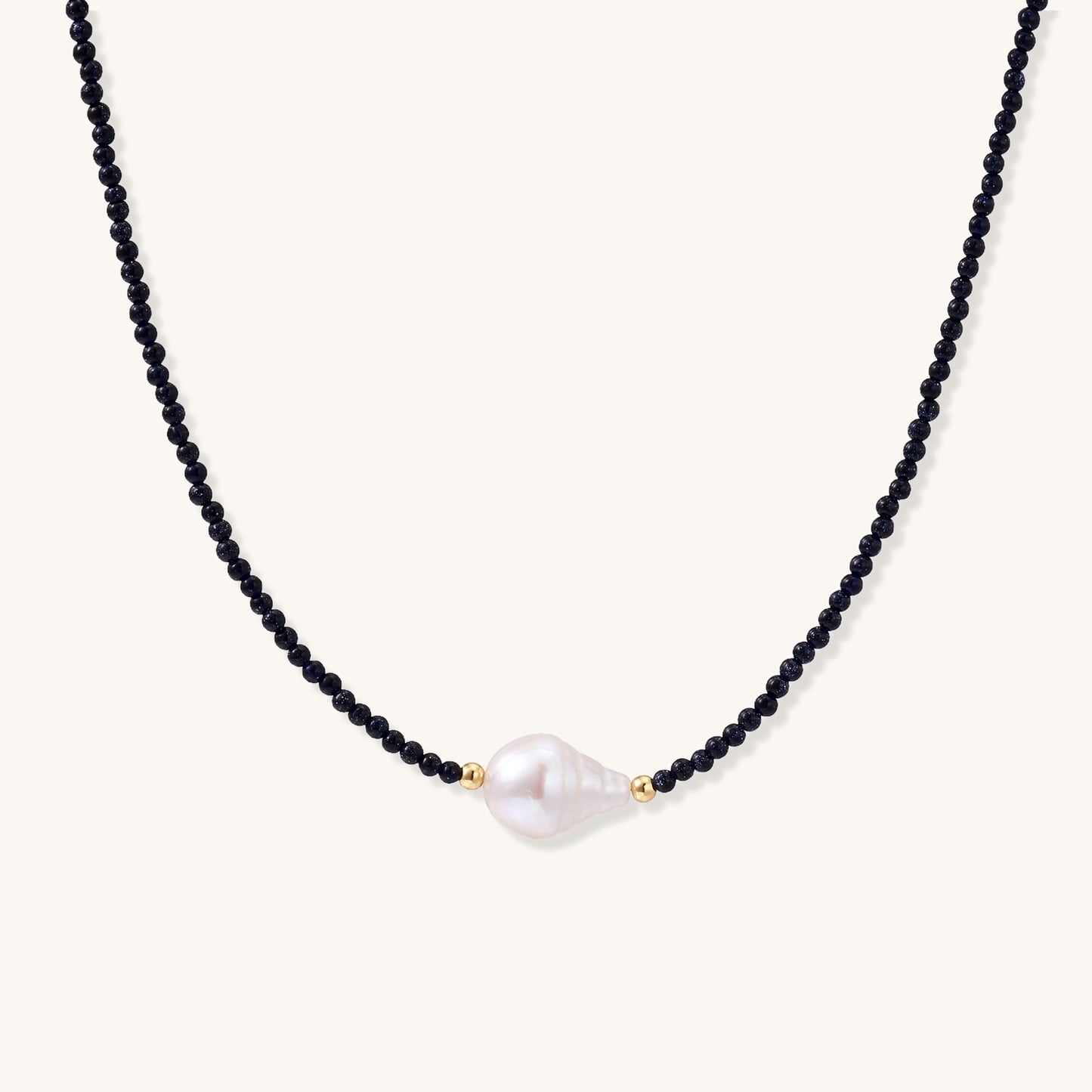 Elegant necklace with blue sandstone beads and baroque pearl centerpiece with gold accents on neutral background.