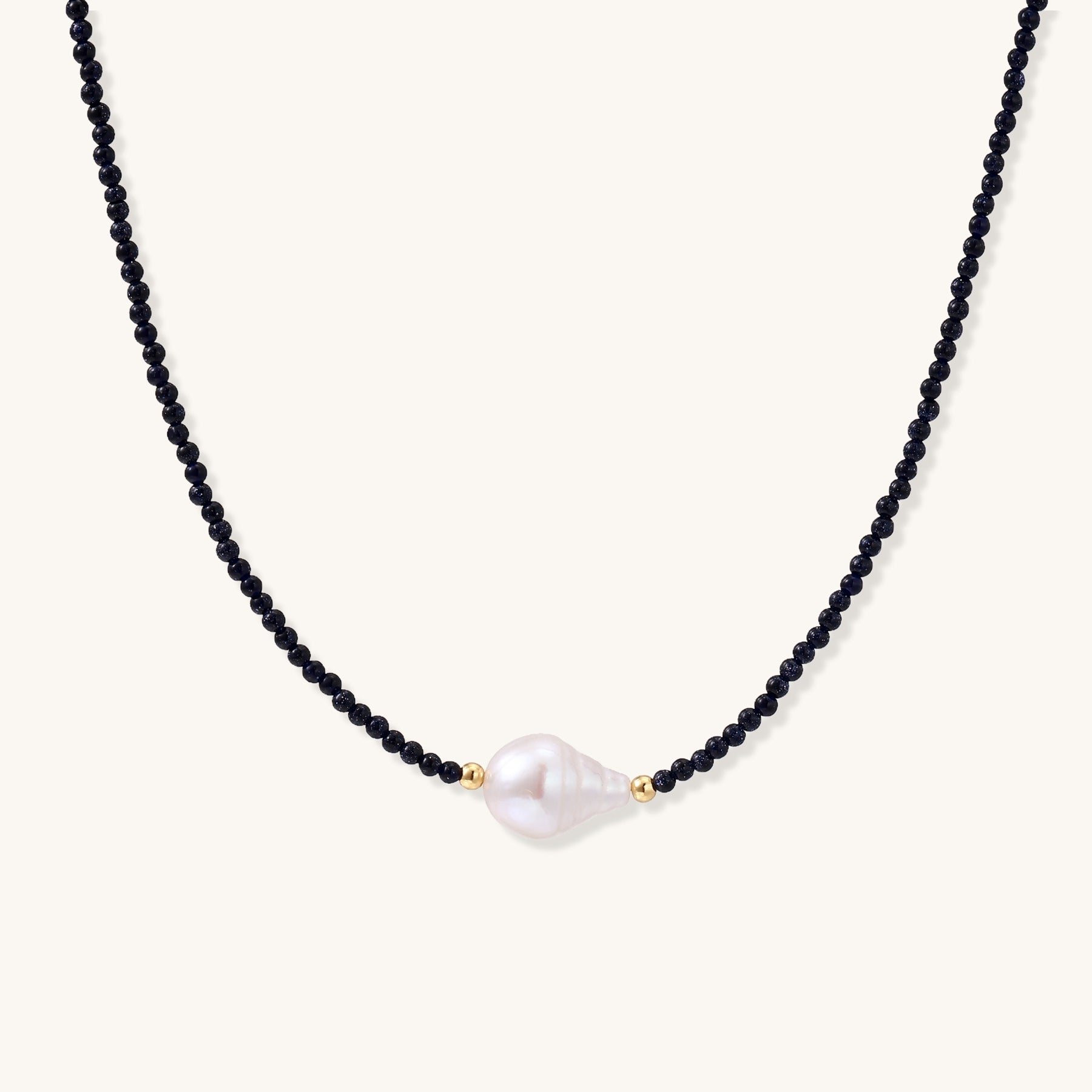 Elegant necklace with blue sandstone beads and baroque pearl centerpiece with gold accents on neutral background.