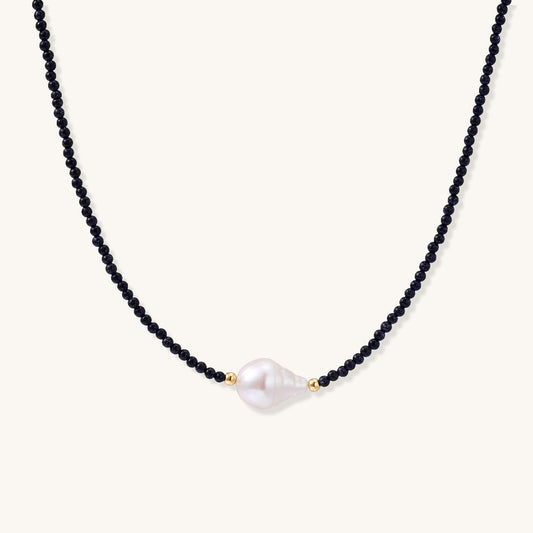 Elegant necklace with blue sandstone beads and baroque pearl centerpiece with gold accents on neutral background.