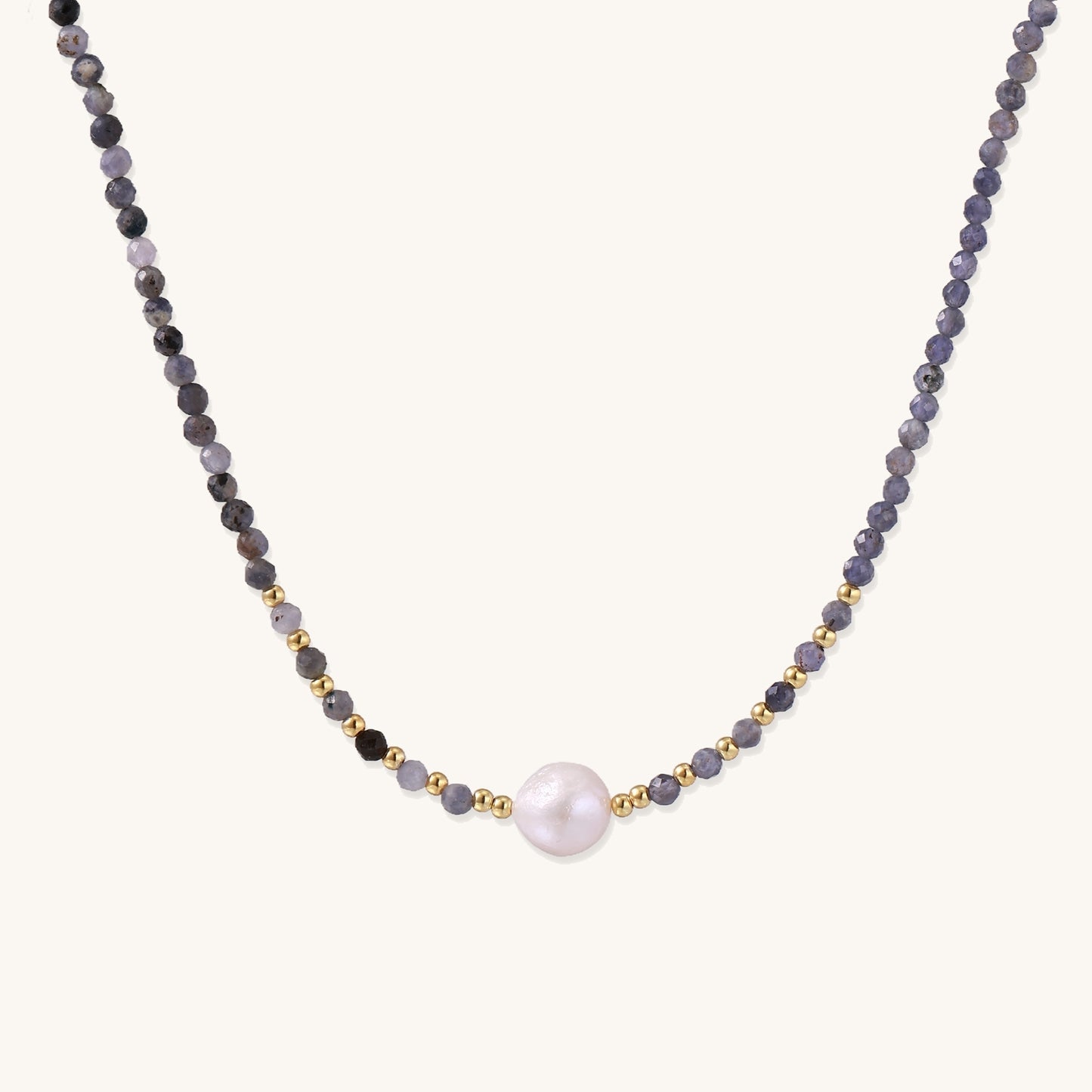 Delicate beaded necklace with violet iolite stones, gold spacers, and central white freshwater pearl on neutral background.