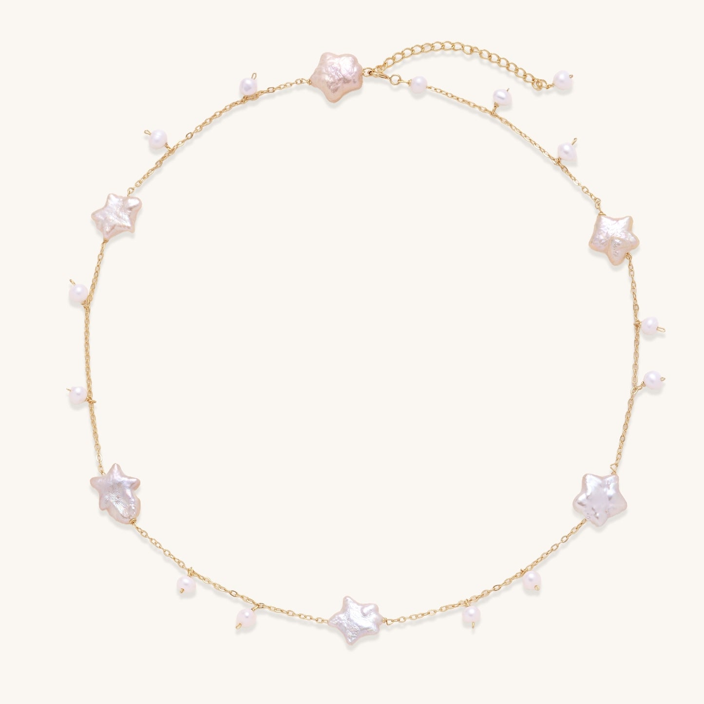 Delicate gold chain necklace with star-shaped baroque pearls and small freshwater pearls on cream background.