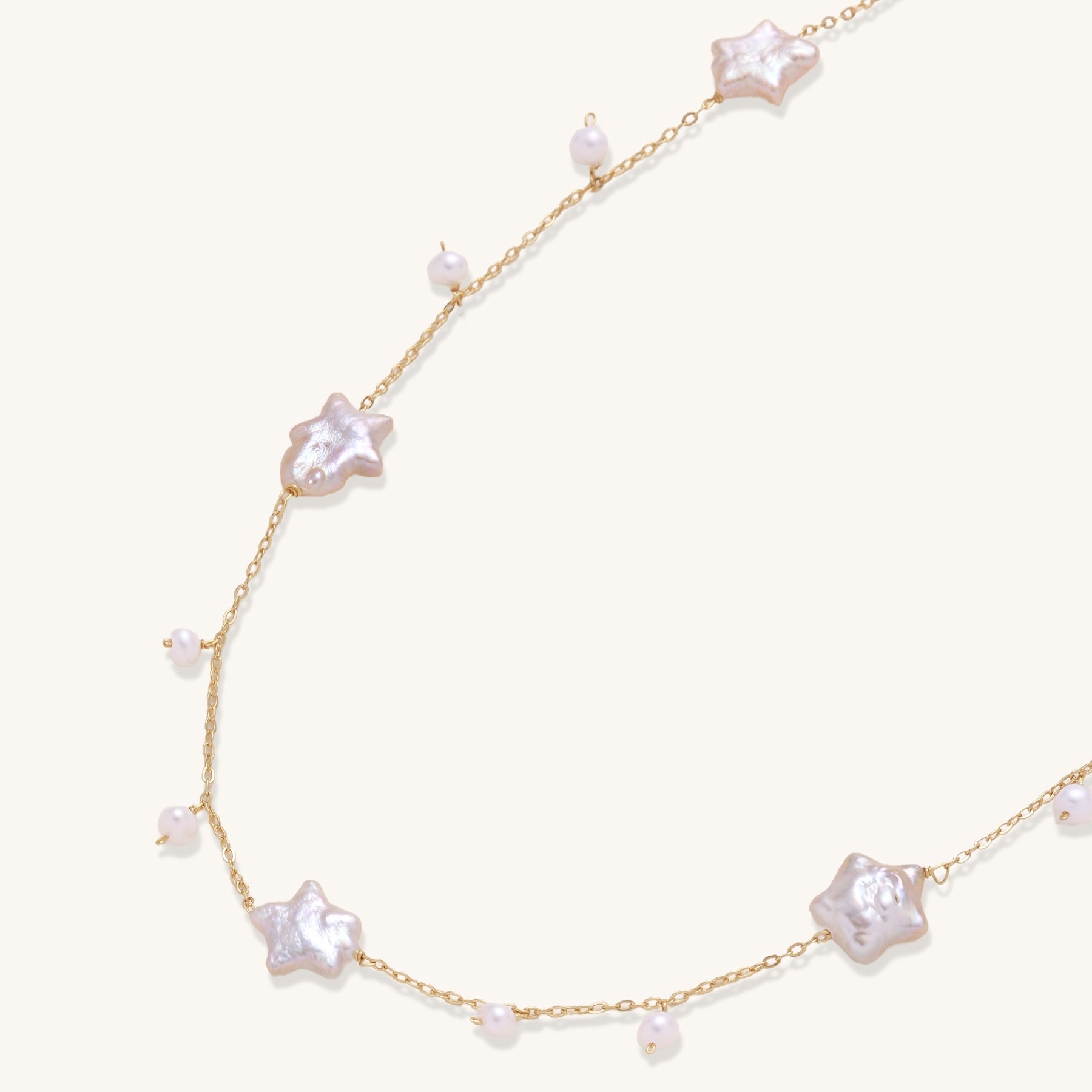 Delicate gold chain necklace with star-shaped baroque pearls and small freshwater pearls on cream background.