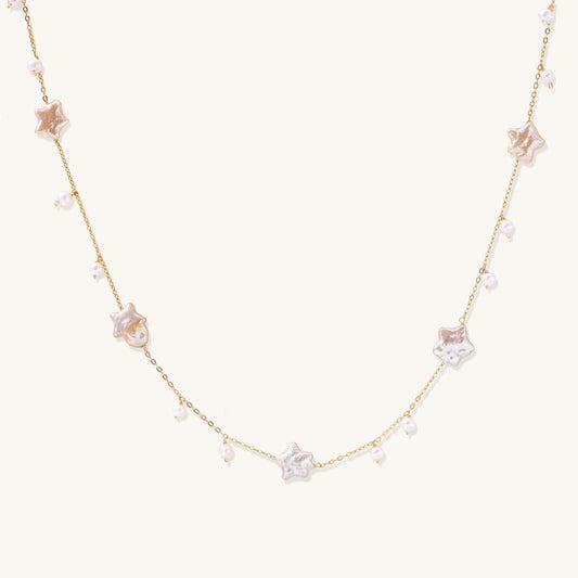 Delicate gold chain necklace with star-shaped baroque pearls and small freshwater pearls on cream background.