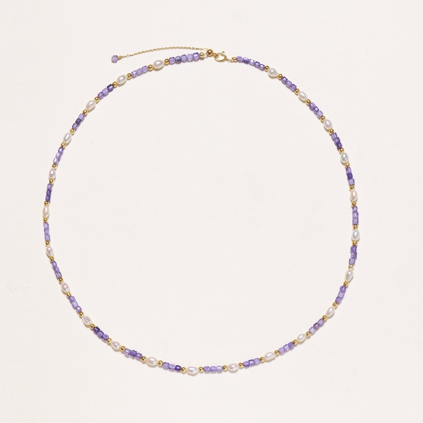 Delicate beaded necklace with alternating purple zirconia stones, white freshwater pearls, and gold-plated spacers on cream background.