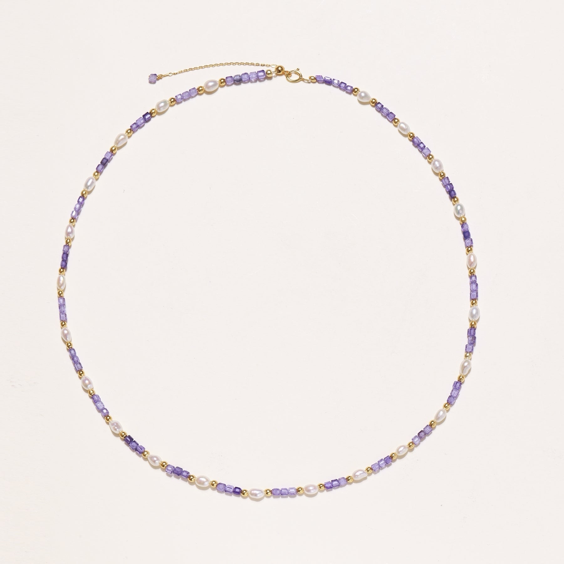 Delicate beaded necklace with alternating purple zirconia stones, white freshwater pearls, and gold-plated spacers on cream background.