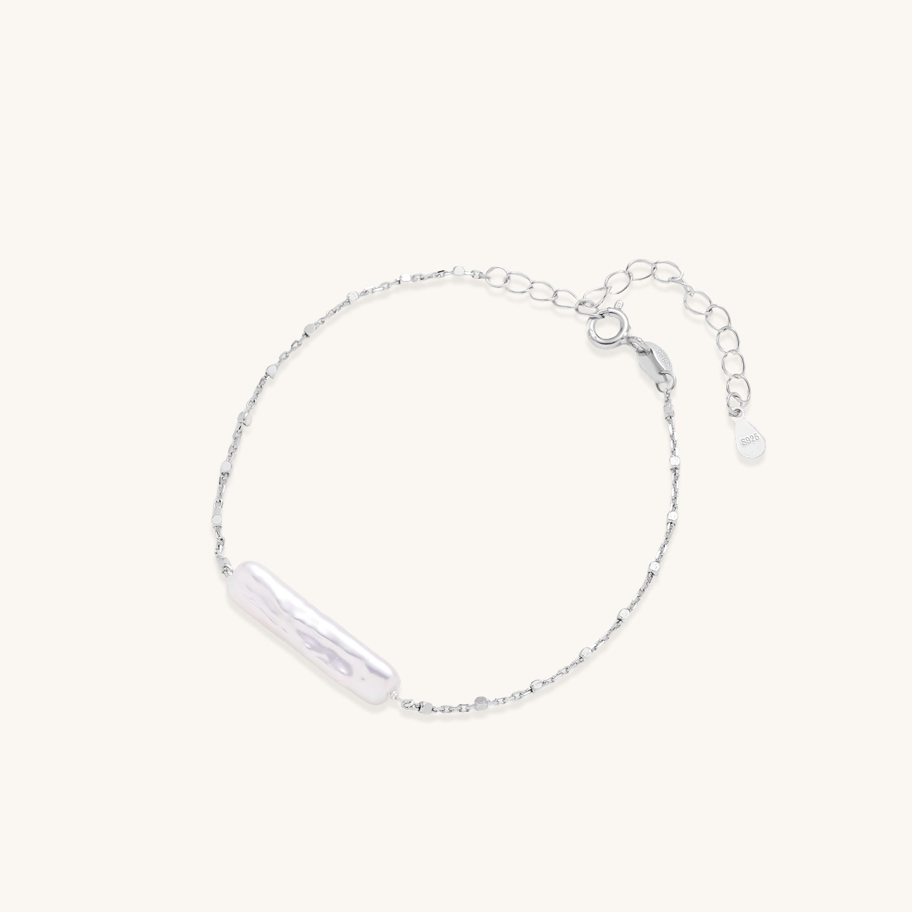 Delicate sterling silver chain bracelet with an organic white baroque pearl centerpiece on neutral background