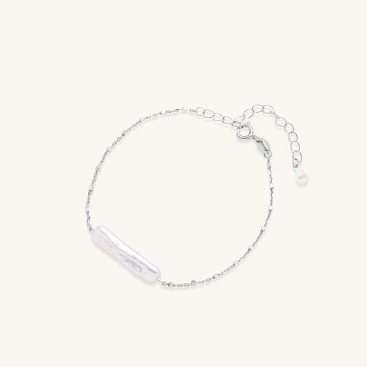 Delicate sterling silver chain bracelet with an organic white baroque pearl centerpiece on neutral background