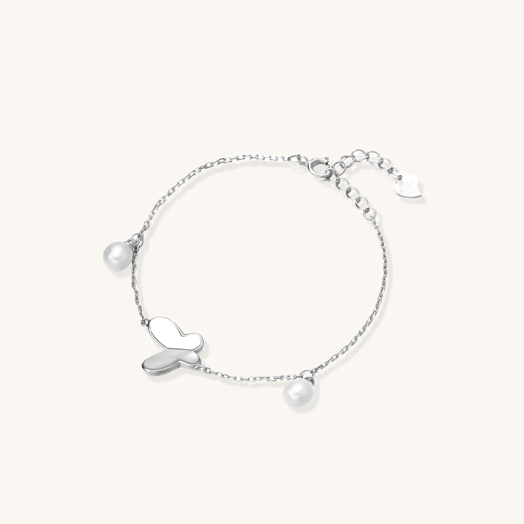 Dainty sterling silver chain bracelet with heart charm and freshwater pearl dangles on white background.