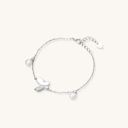 Dainty sterling silver chain bracelet with heart charm and freshwater pearl dangles on white background.