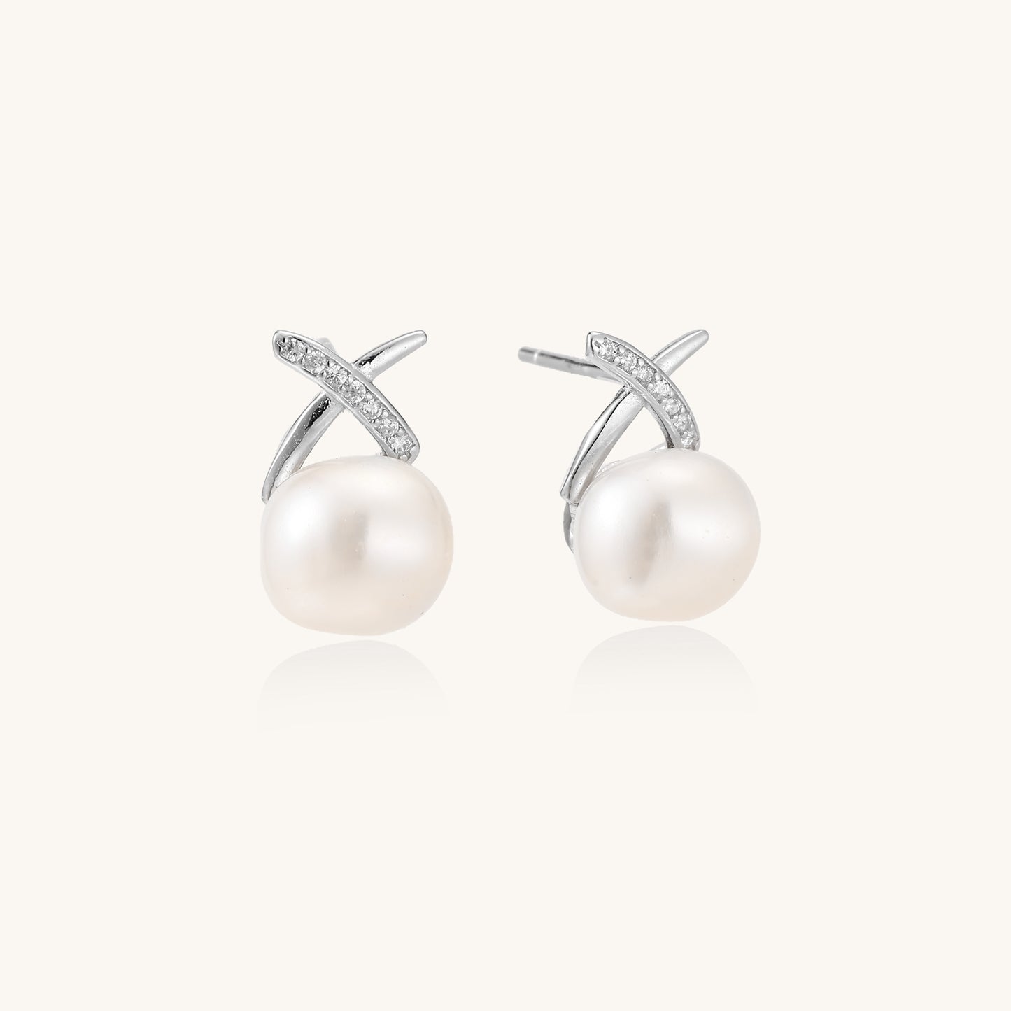 Sterling silver cross-shaped stud earrings with round freshwater pearls dangling below on white background.