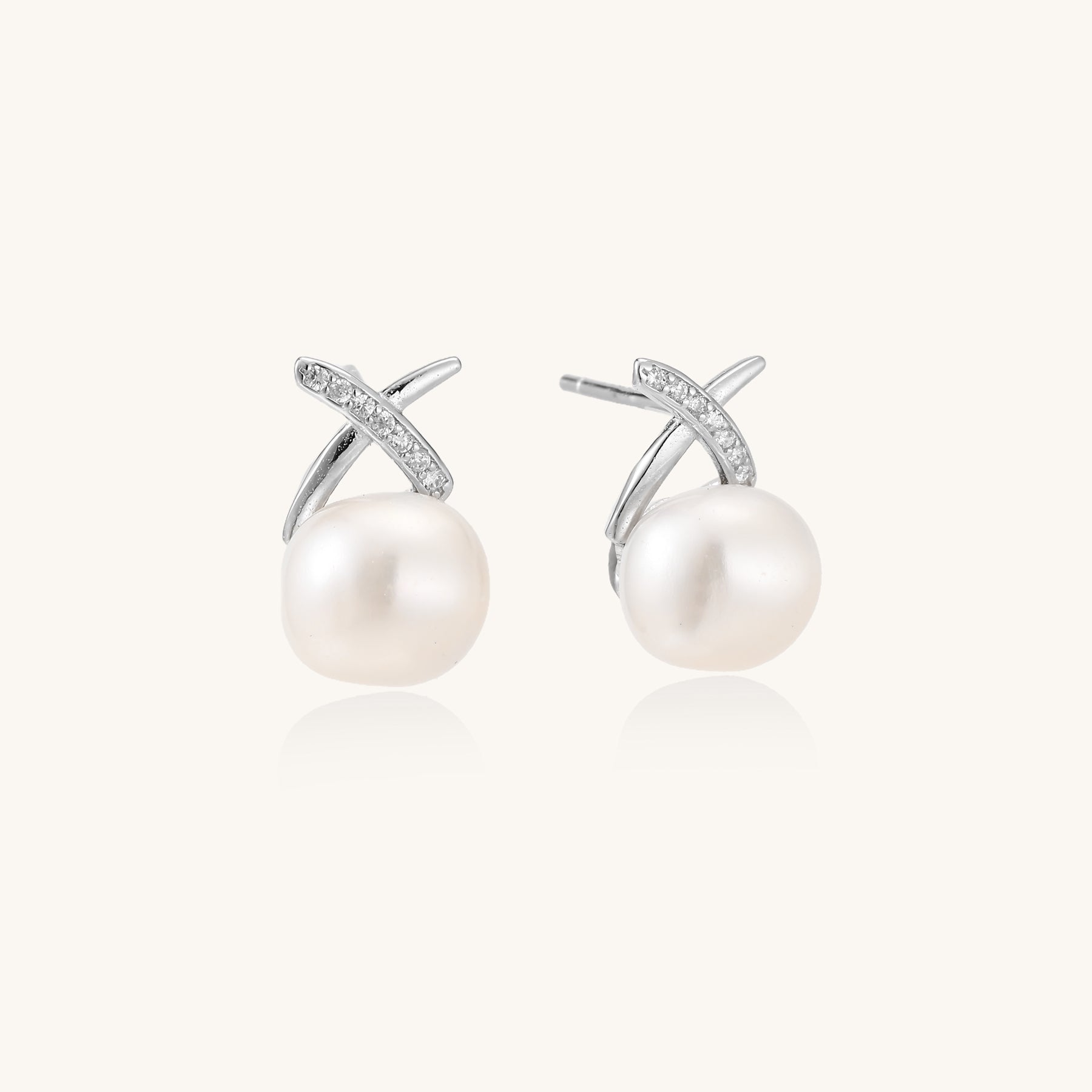 Sterling silver cross-shaped stud earrings with round freshwater pearls dangling below on white background.