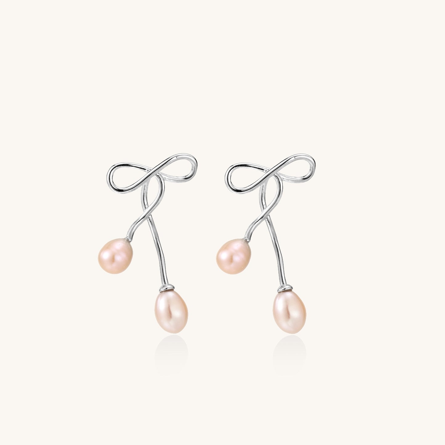 Delicate sterling silver wire earrings with organic bow shapes and two pink freshwater pearls on white background